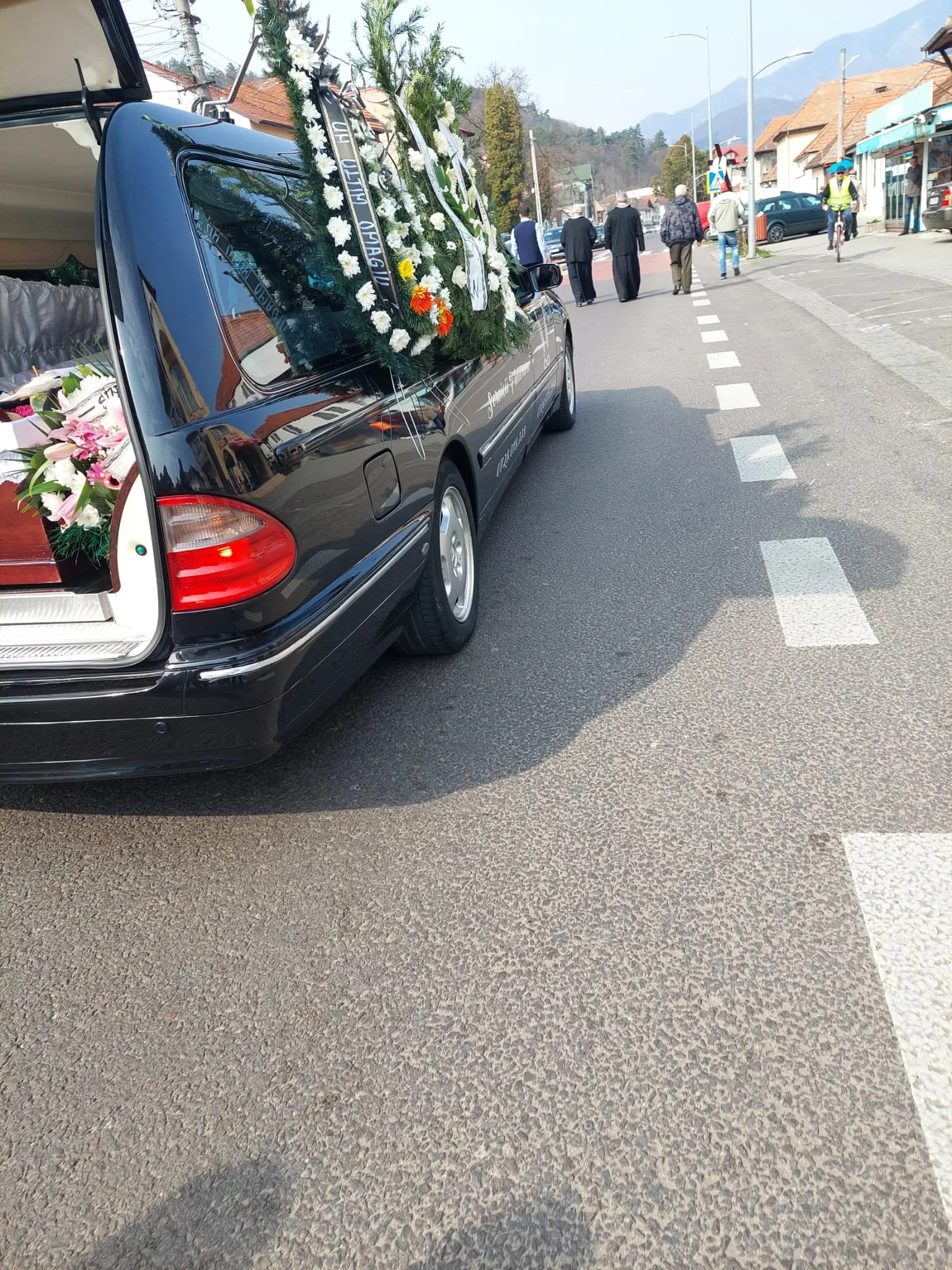 Autovehicul funerar cu coroane funerare pe drum